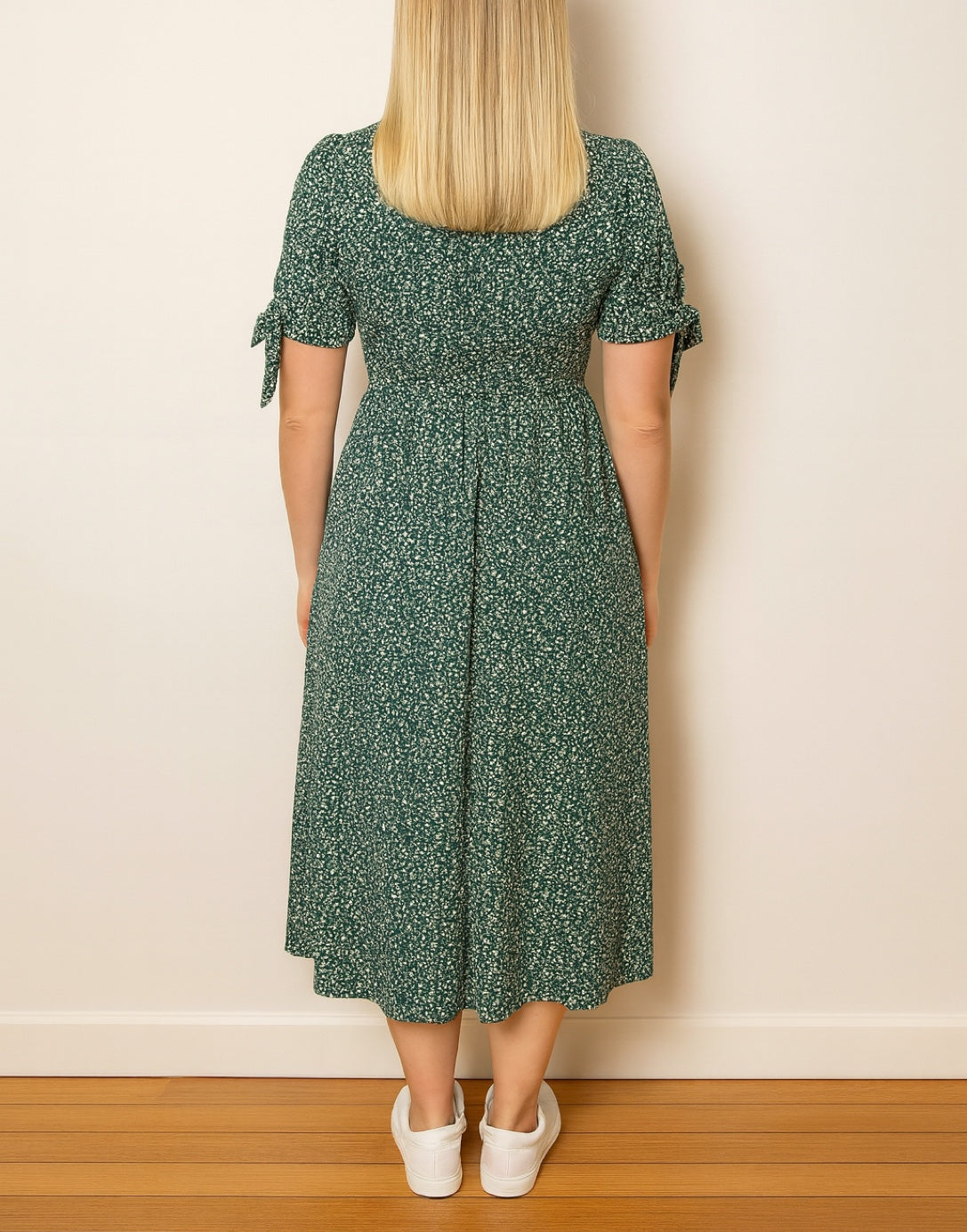 Back view of woman wearing a green floral Tie Sleeve Button Front Midi Dress against a plain wall.