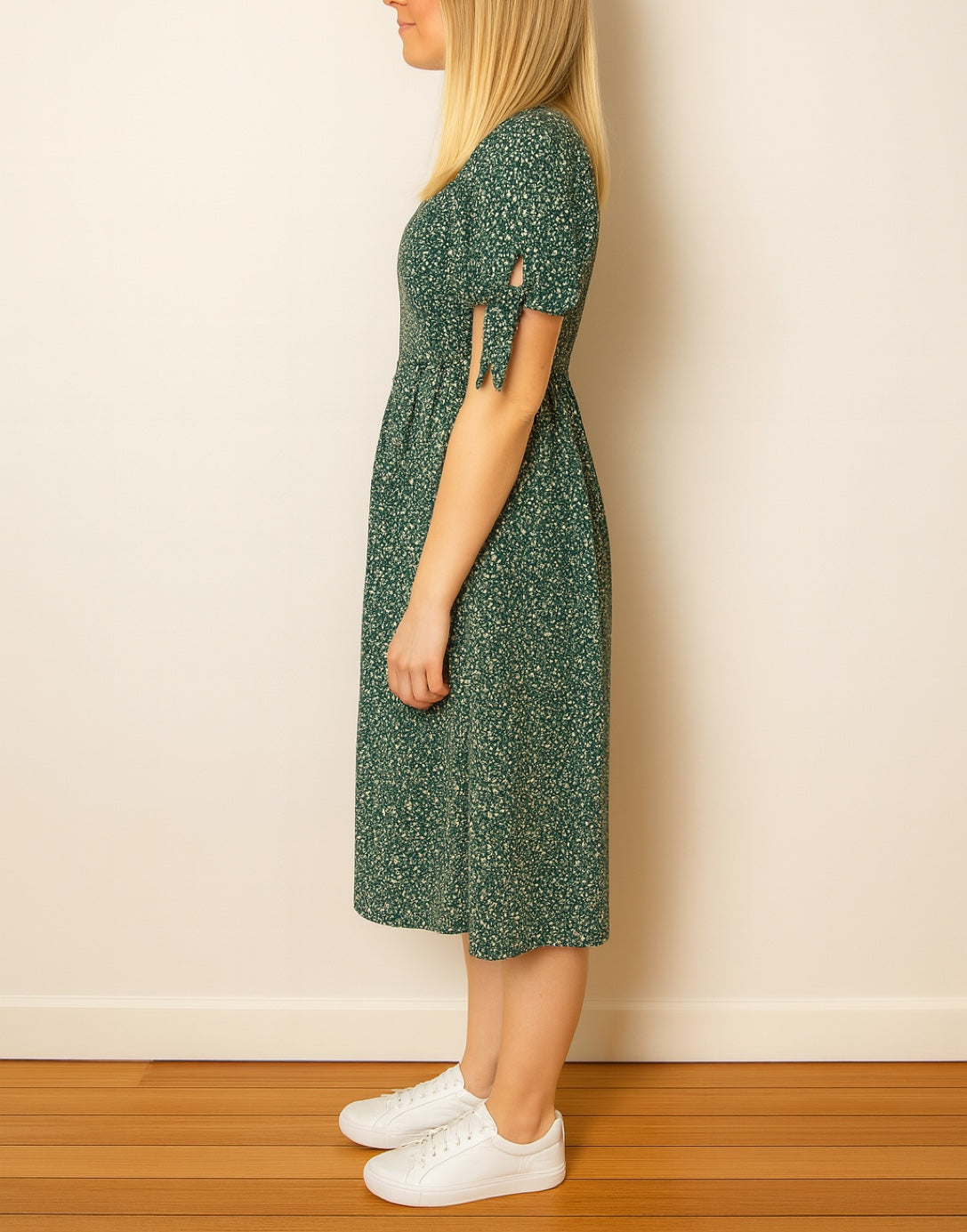 Side view of woman wearing a green floral Tie Sleeve Button Front Midi Dress standing in front of plain wall.
