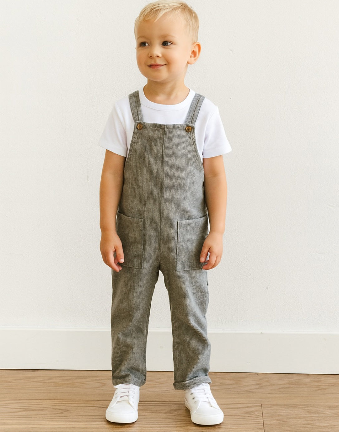 Child wearing gray overalls and a white shirt on a plain background