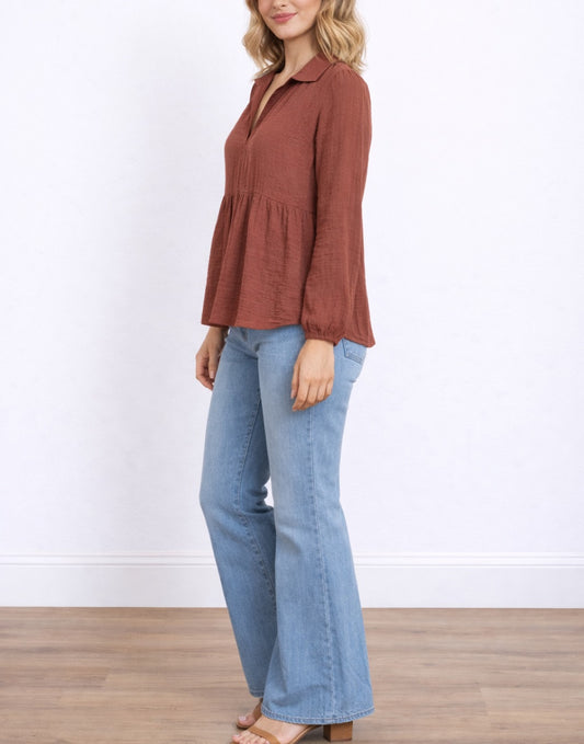 Side view of woman wearing a rust-colored V-Neck Gathered Babydoll Blouse and blue jeans on a white background.