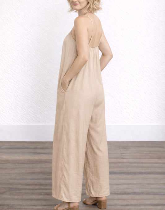 Side view of woman wearing a beige Wide Leg Cami Jumpsuit against a white wall.