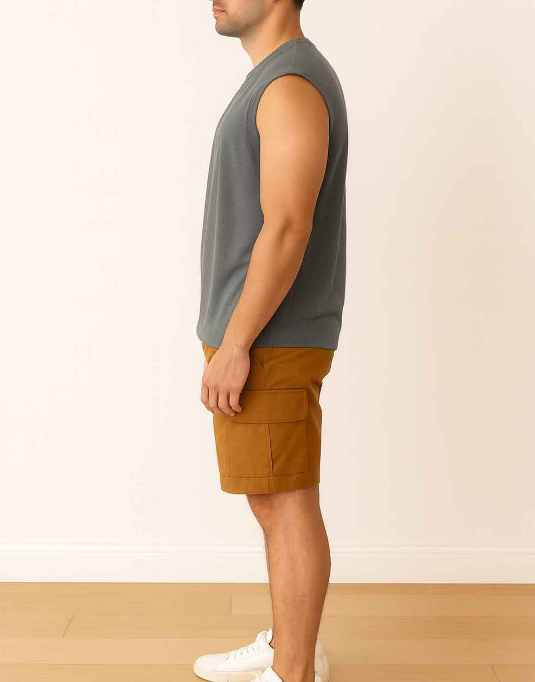 Side view of man wearing a dark gray Wide Shoulder Tank Top with brown shorts and white shoes on a wooden floor.