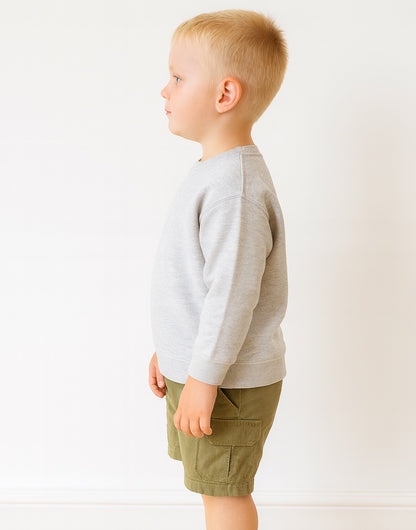 Side view of young boy wearing a gray sweatshirt and green shorts on a white background