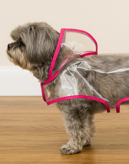 Side view of dog wearing a transparent Hooded Raincoat with pink trim on a wooden floor.