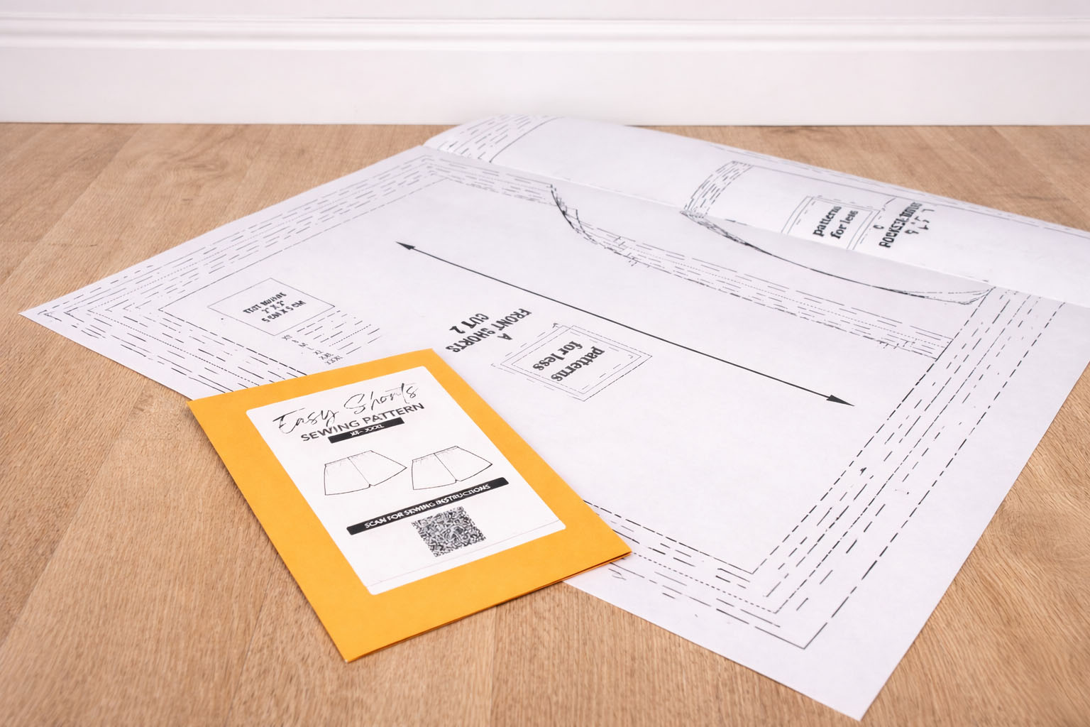 Sample of paper sewing pattern and a yellow envelope with a label on a wooden surface