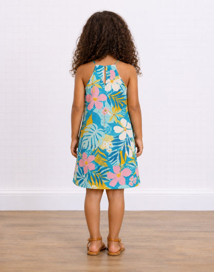 A young girl with curly brown hair is shown from behind wearing a Sleeveless Halter A-line Dress with a vibrant tropical floral print. The dress features a turquoise blue background with pink, white, and yellow flowers and green leaves.