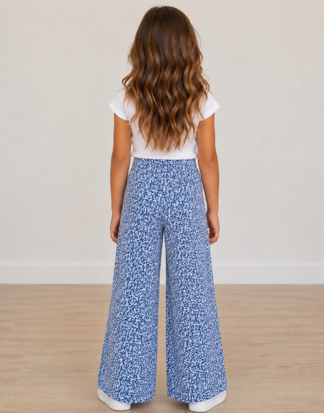 Back view of young girl wearing a white top and blue floral High Waist Pants on a plain background.