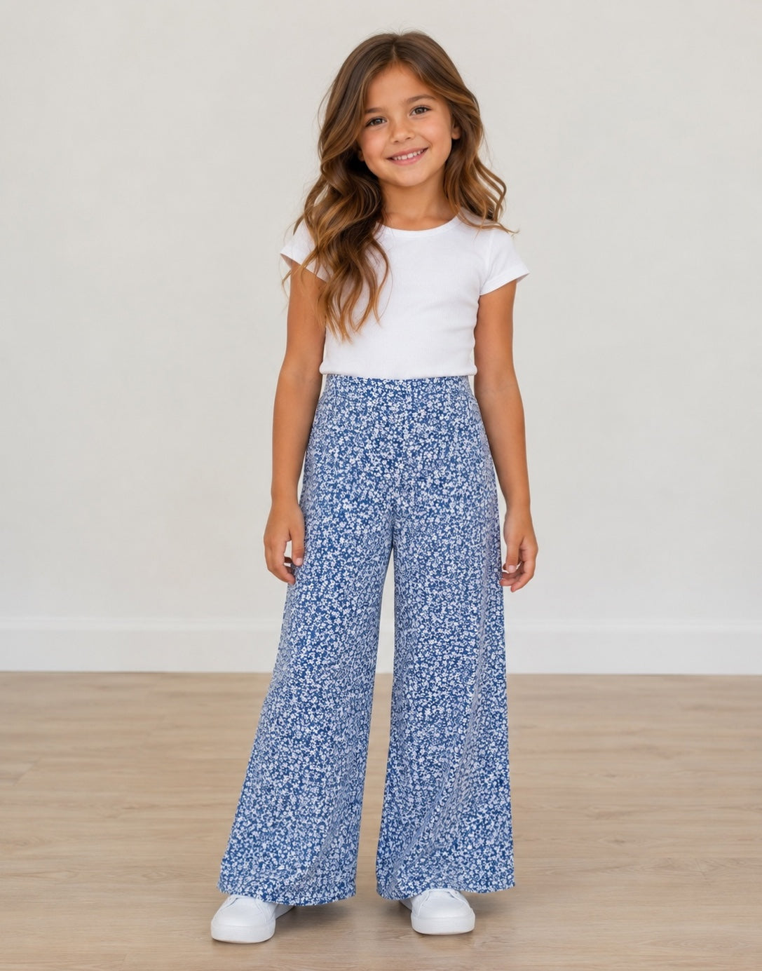 Young girl wearing a white top and blue floral High Waist Pants on a plain background