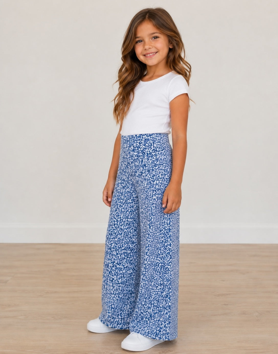 Side view of young girl wearing a white top and blue floral High Waist Pants on a plain background.