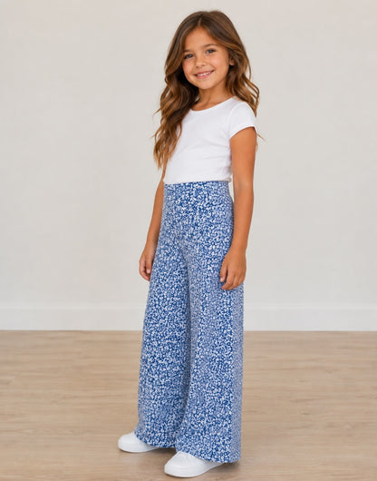 Side view of young girl wearing a white top and blue floral High Waist Pants on a plain background.