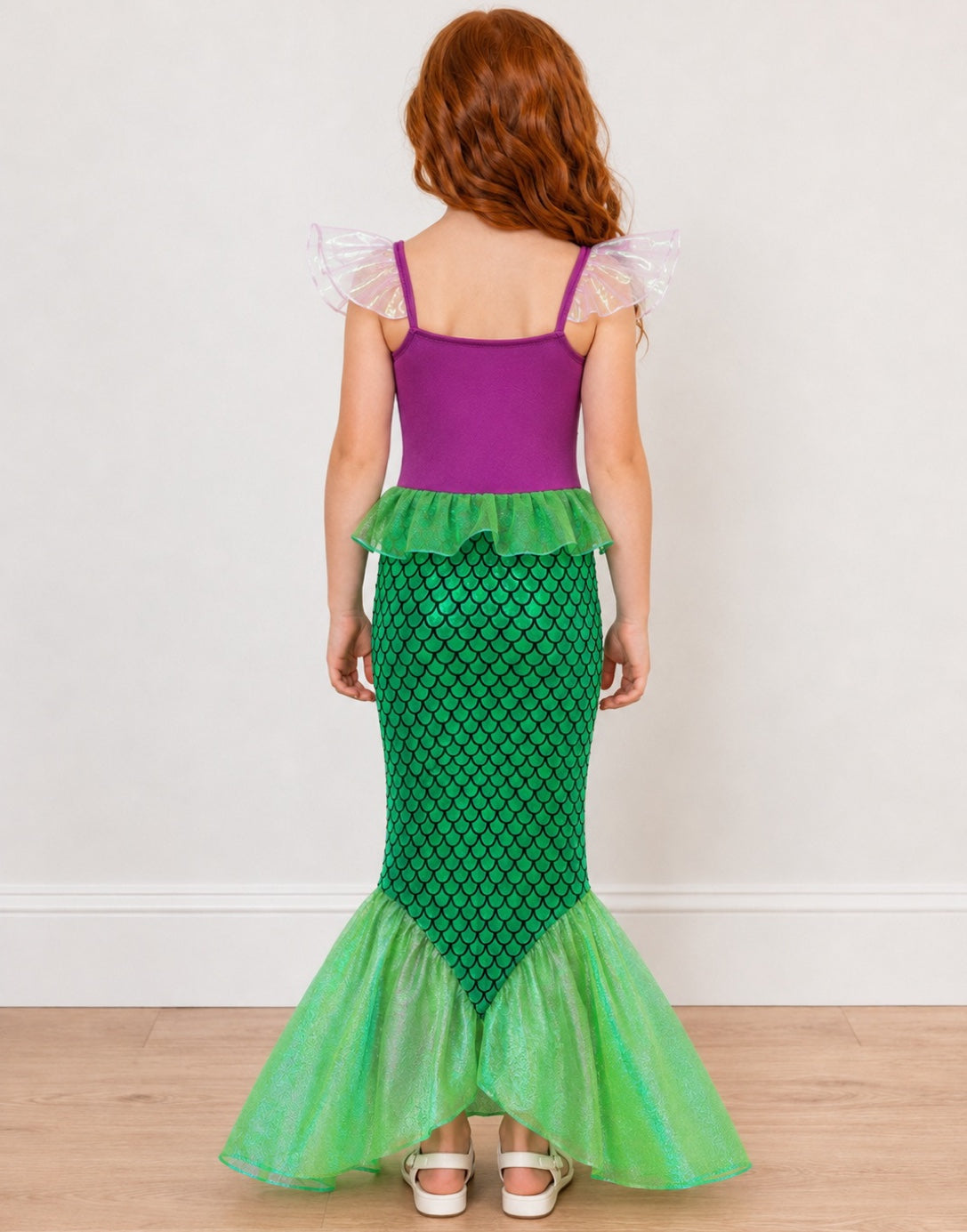 A young girl shown from the back wearing a Mermaid Costume. The costume features a purple top with sheer white ruffled shoulder straps, a green ruffle waistband, and a green scale-patterned mermaid tail with a sheer lime green flared fin.