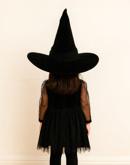 Back view of person wearing a black witch costume with a pointed Witch Hat on a plain background.