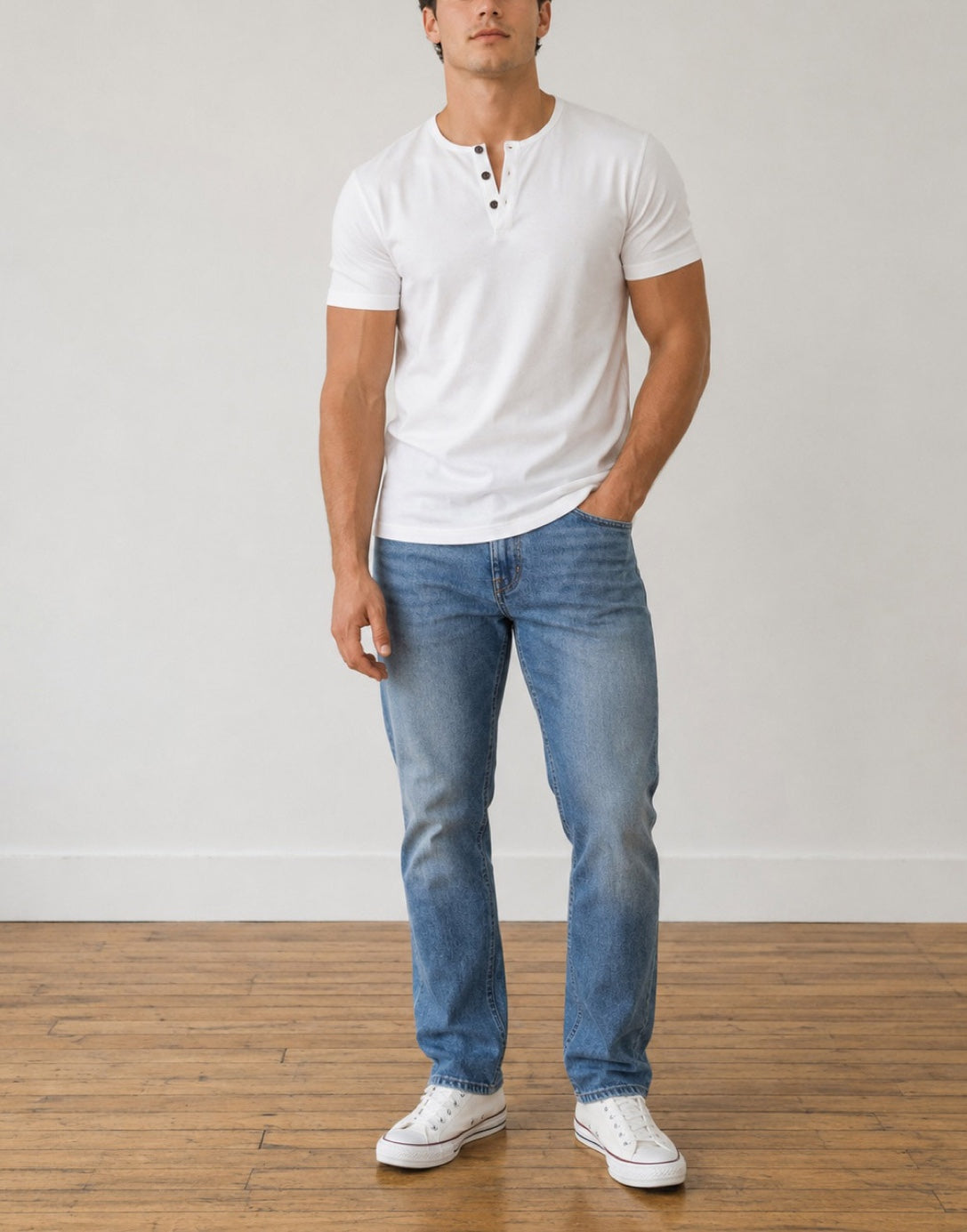 A man modeling a white Button Front Short-Sleeve Henley T-Shirt, blue jeans, and white sneakers, standing against a white wall on a wooden floor.