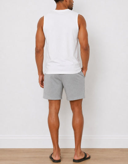 A man shown from the back wearing a white sleeveless t-shirt and light gray heathered Sweat Shorts, standing against a white wall on a light wood floor.