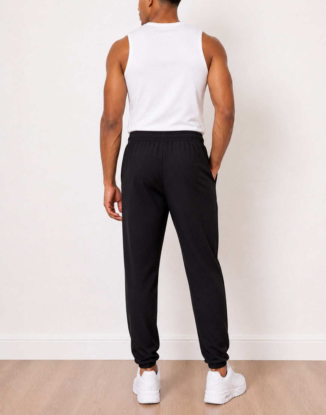 Back view of man wearing a white tank top and black Jogger Pants with white sneakers against a white background.