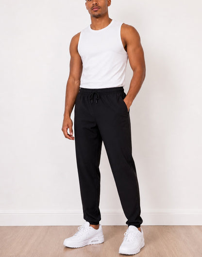 Man wearing a white tank top and black Jogger Pants with white sneakers against a white background
