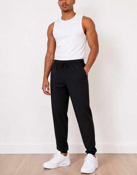 Man wearing a white tank top and black Jogger Pants with white sneakers against a white background