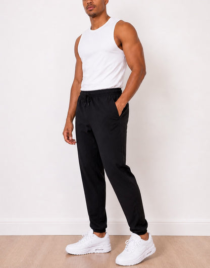 Side view of man wearing a white tank top and black Jogger Pants with white sneakers against a white background.