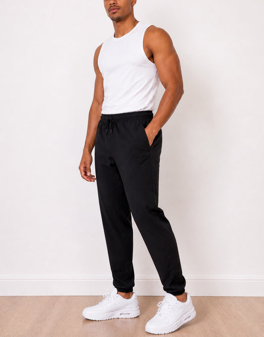 Side view of man wearing a white tank top and black Jogger Pants with white sneakers against a white background.