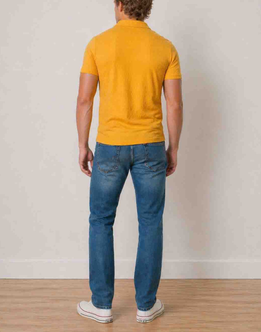 Back view of man wearing a yellow Knit Short Sleeve Polo Shirt and blue jeans standing against a plain background.