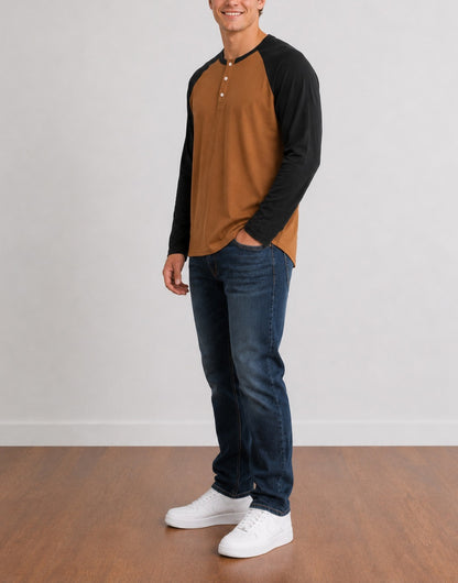 Side view of a man wearing a brown and black Raglan Long Sleeve Henley Top, dark blue jeans, and white sneakers, standing against a light gray wall and wood floor.
