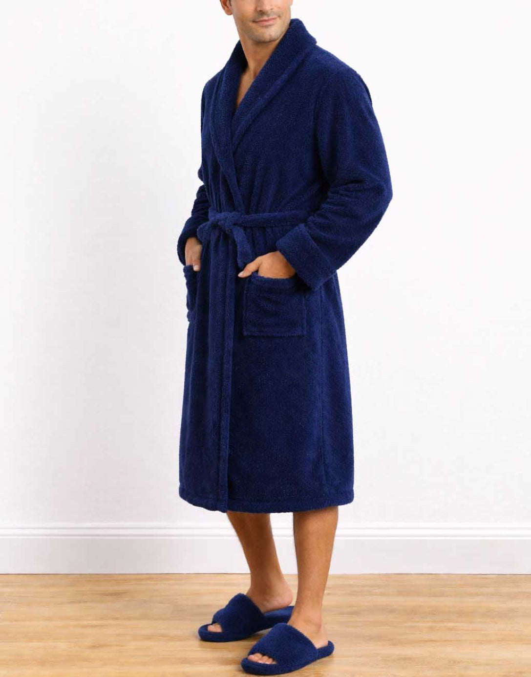 Side view of man wearing a blue Shawl Collar Bathrobe and matching slippers on a white background.