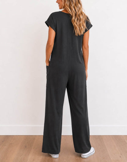 Back view of woman wearing a charcoal gray Oversized Knit Tee Jumpsuit with white shoes on a wooden floor with a plain background.