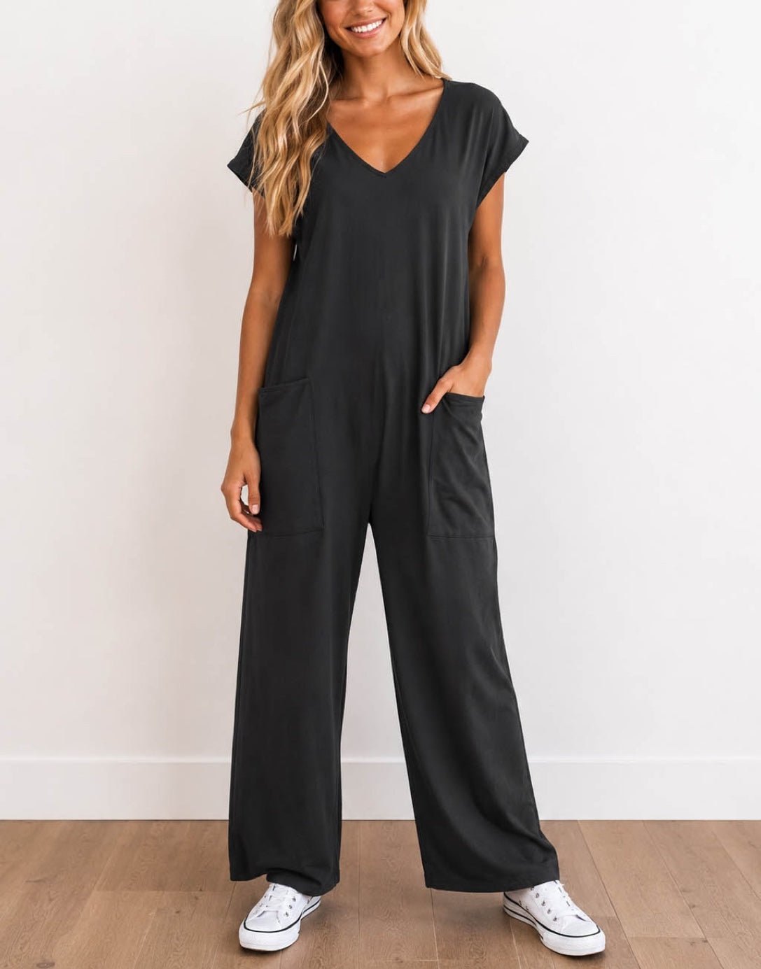Woman wearing a charcoal gray Oversized Knit Tee Jumpsuit with white shoes on a wooden floor with a plain background.