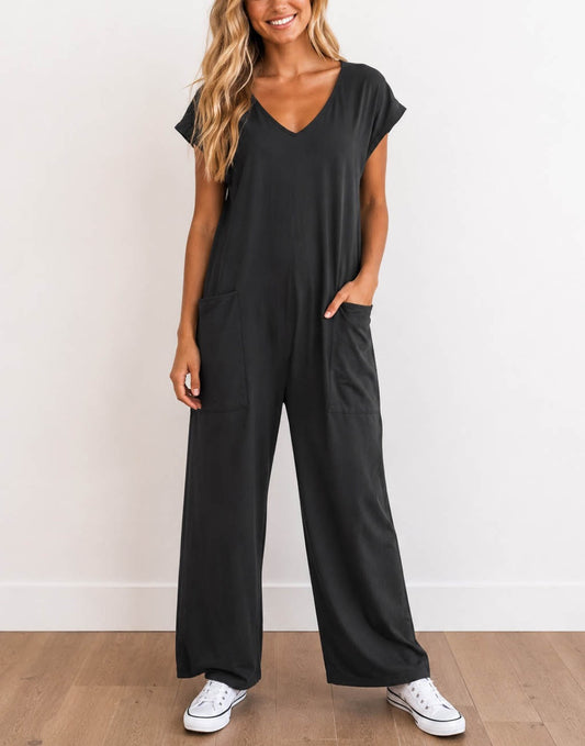 Woman wearing a charcoal gray Oversized Knit Tee Jumpsuit with white shoes on a wooden floor with a plain background.