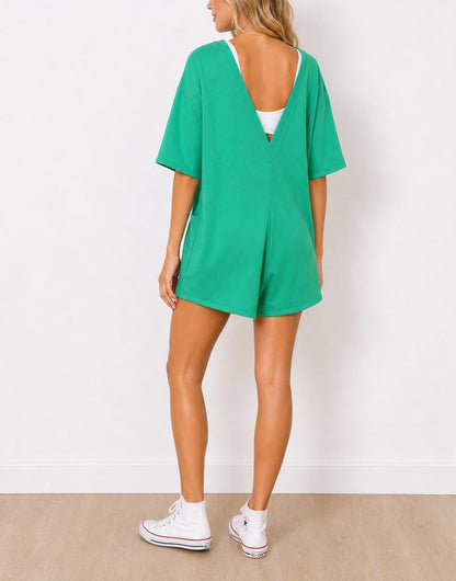 Back view of woman wearing a green Oversized Tee Romper and white sneakers on a plain background