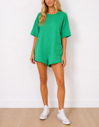 Woman wearing a green Oversized T-Shirt Romper and white sneakers on a plain background