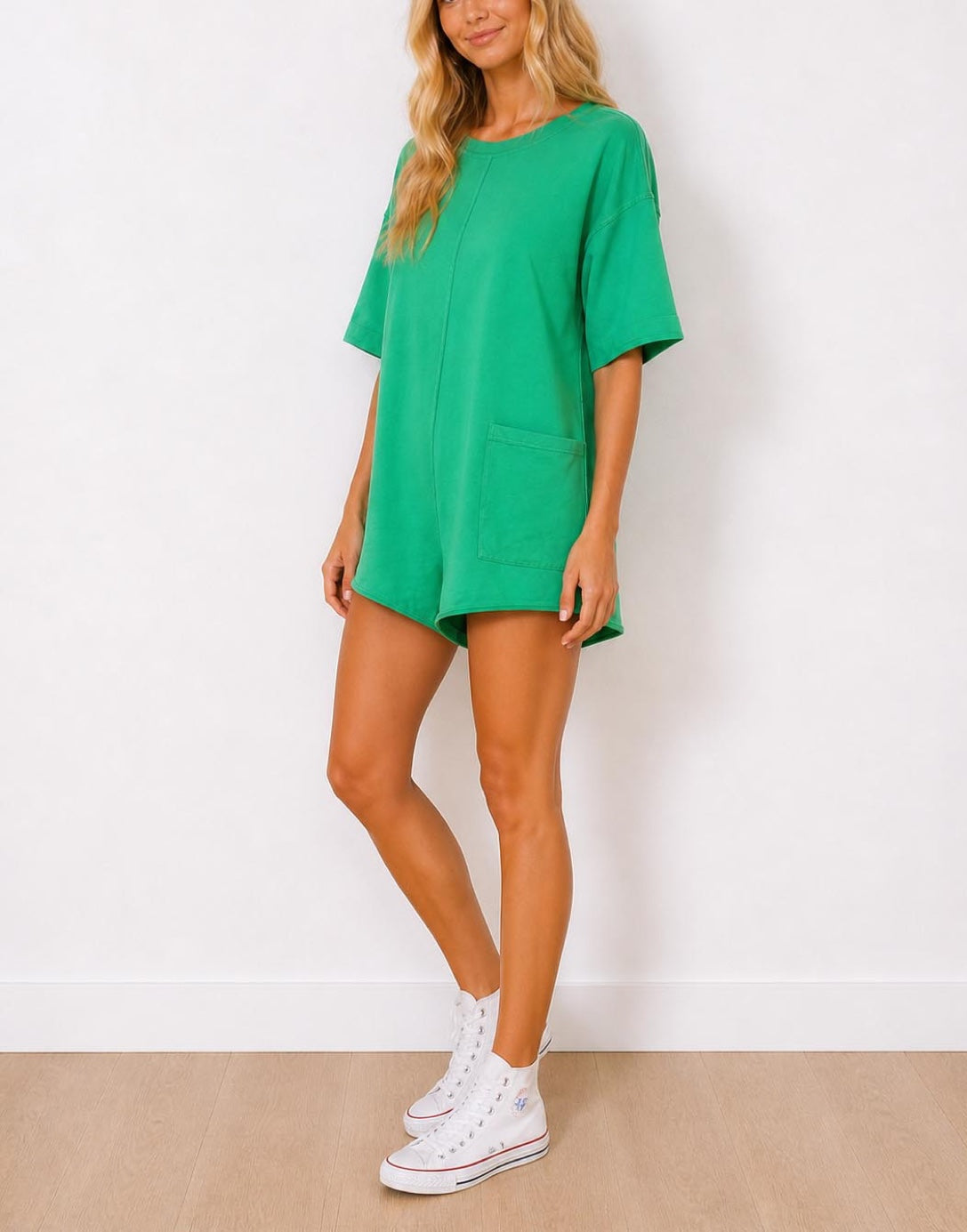 Side view of woman wearing a green Oversized Tee Shirt Romper and white sneakers on a plain background