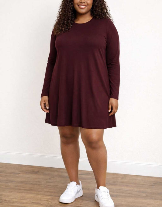 Woman wearing a burgundy long-sleeve dress with white sneakers on a plain background