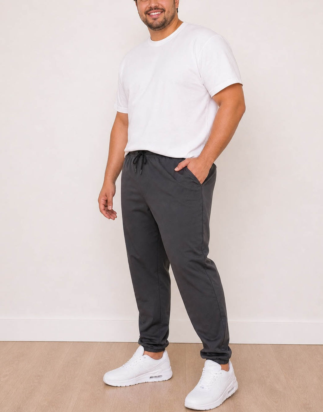Side view of man wearing a white t-shirt and dark gray Plus Size Mens Jogger against a plain background.