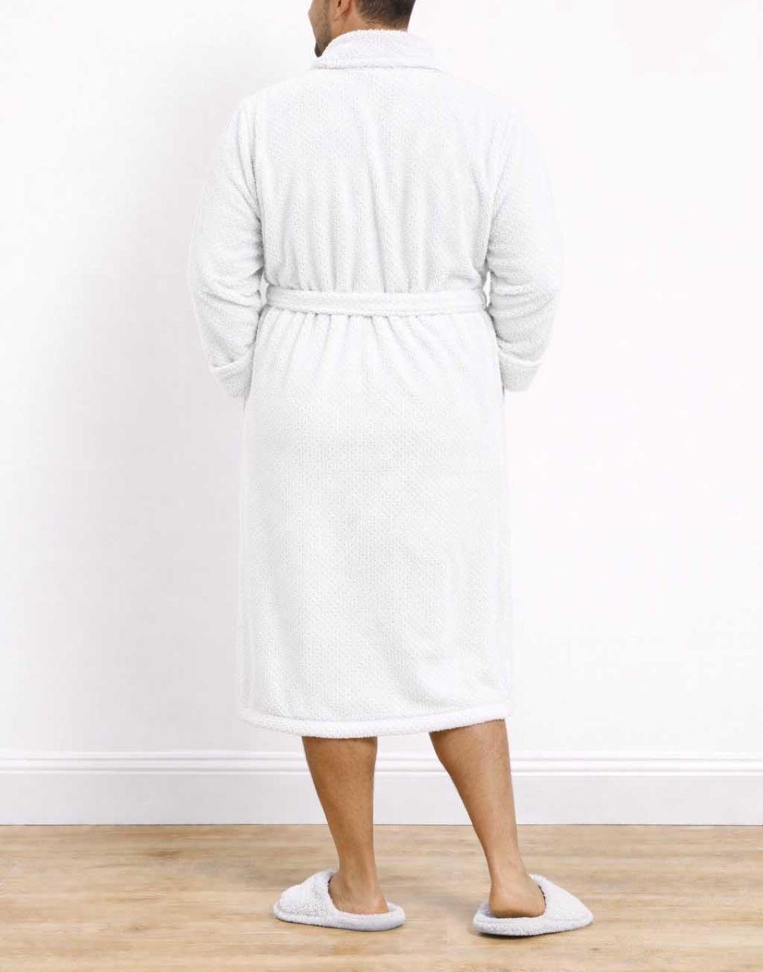 Back view of man wearing a white Plus Size Mens Shawl Collar Bathrobe and slippers on a wooden floor with a white wall background.