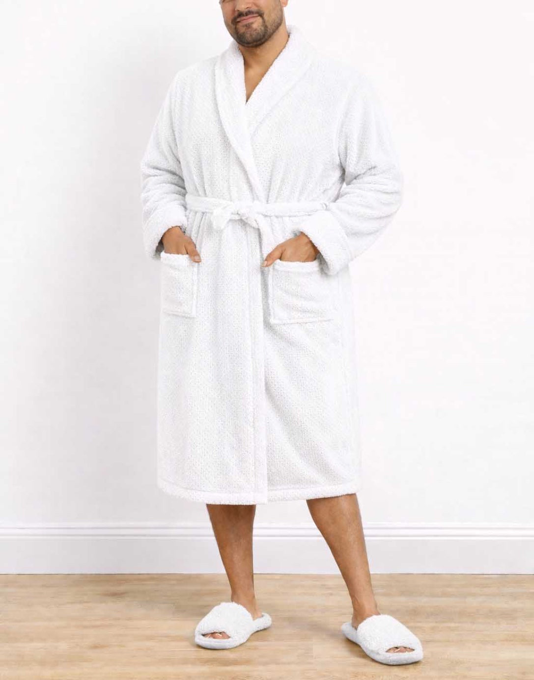 Man wearing a white Plus Size Mens Shawl Collar Bathrobe and slippers on a wooden floor with a white wall background