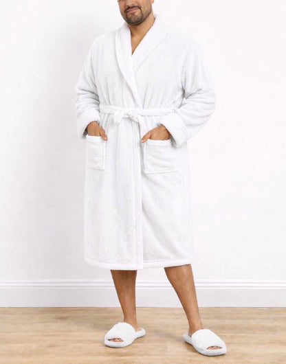 Man wearing a white Plus Size Mens Shawl Collar Bathrobe and slippers on a wooden floor with a white wall background