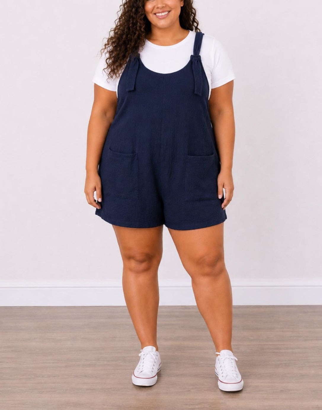 Woman wearing navy blue Plus Size Overall Romper with a white shirt underneath on a plain background