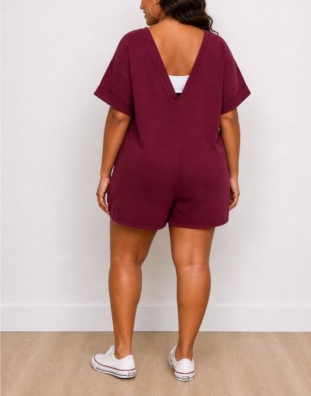 Back view of woman wearing a maroon Plus Size Oversized Tee Romper with white sneakers against a white background.