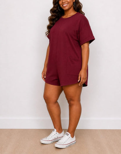 Side view of woman wearing a maroon Plus Size Oversized Tee Romper with white sneakers against a white background.