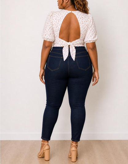 Back view of woman wearing a white floral Plus Size Puff Sleeve Open Back Tie Crop Blouse and dark blue jeans against a plain background.