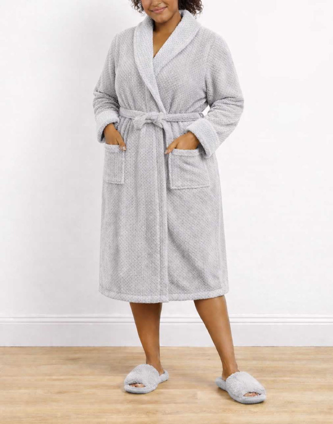 Woman wearing a gray Plus Size Shawl Collar Bathrobe and slippers on a wooden floor with a white wall background