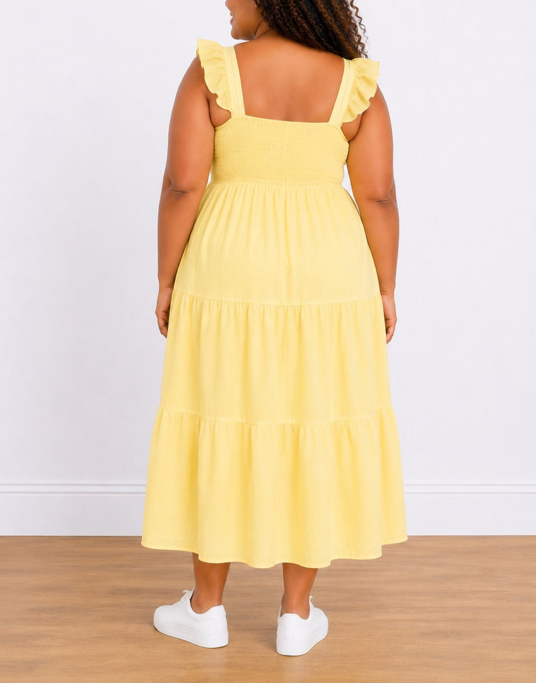 Back view of woman wearing a yellow Plus Size Shirred Maxi Dress with white sneakers on a wooden floor.