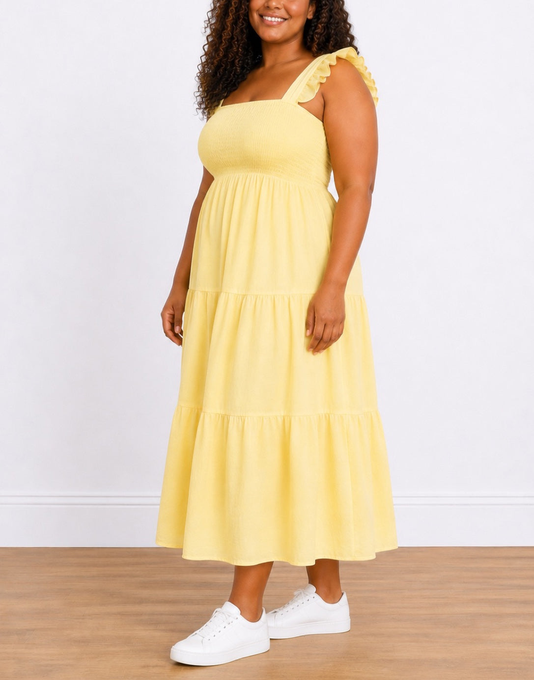 Side view of woman wearing a yellow Plus Size Shirred Maxi Dress with white sneakers on a wooden floor.