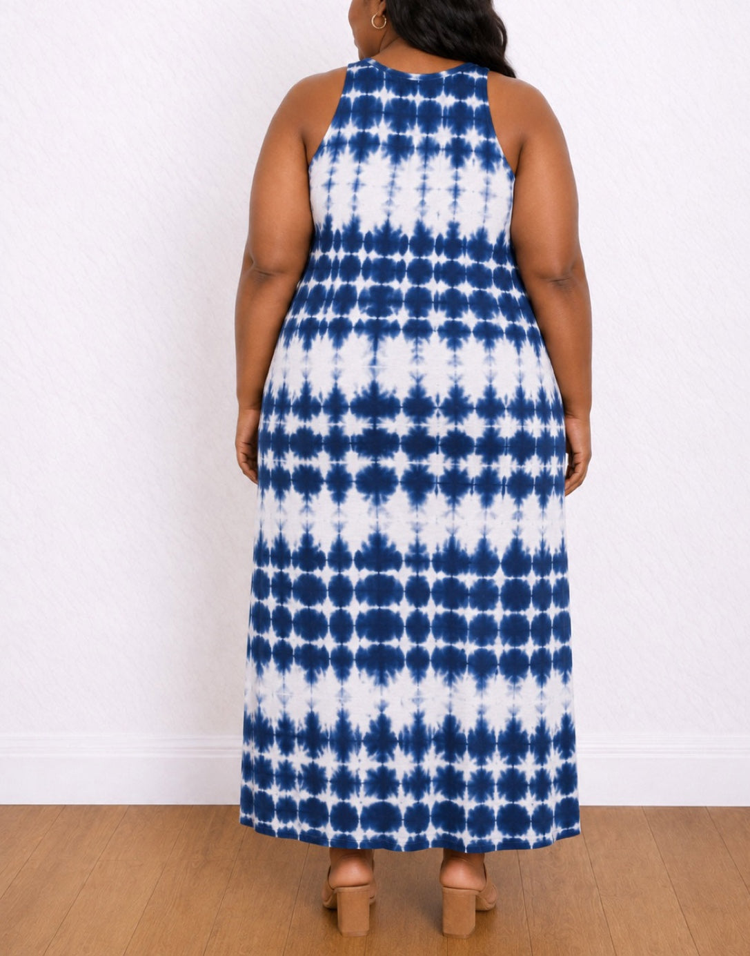 Back view of a woman modeling a Sleeveless Maxi Tank Dress with a blue and white tie-dye pattern and a side slit, standing against a white wall on a wood floor.