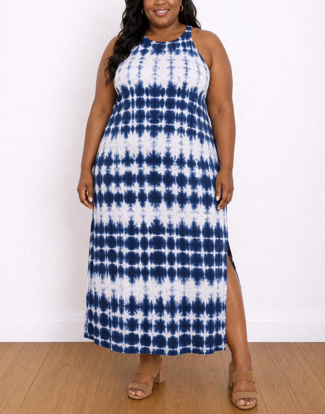 A woman modeling a Sleeveless Maxi Tank Dress with a blue and white tie-dye pattern and a side slit, standing against a white wall on a wood floor.