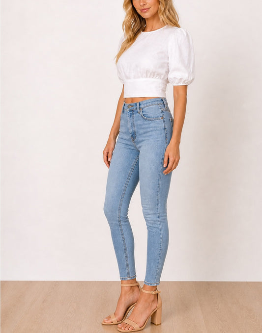 Side view of woman wearing a white Puff Sleeve Open Back Tie Crop Blouse and light blue jeans against a white background.