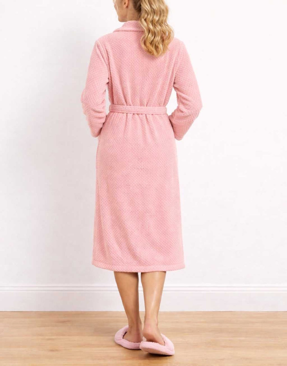 Back view of woman wearing a pink Shawl Collar Bathrobe and matching slippers on a wooden floor.