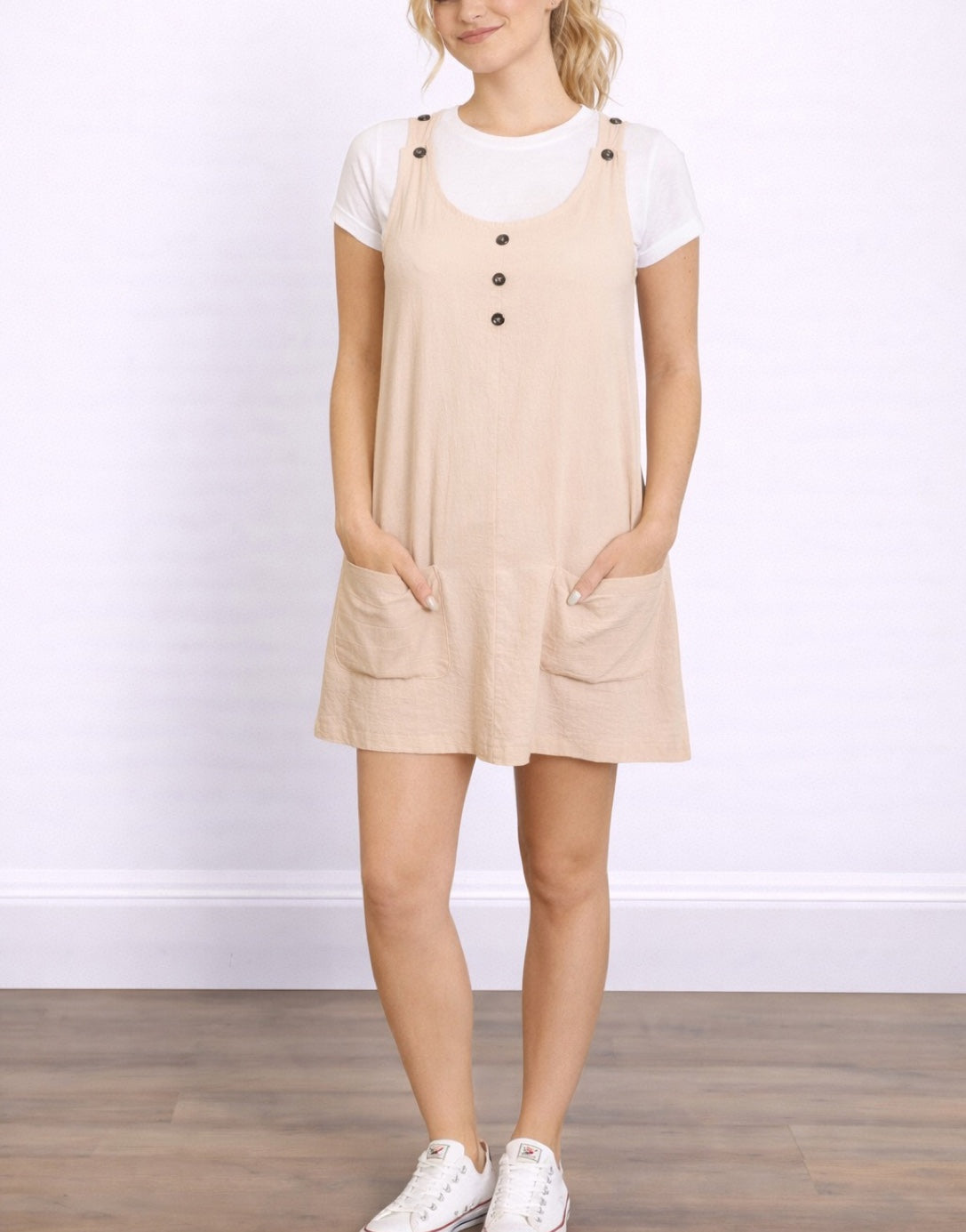 Woman wearing a beige Sleeveless Suspender Shift Dress over a white shirt on a plain background