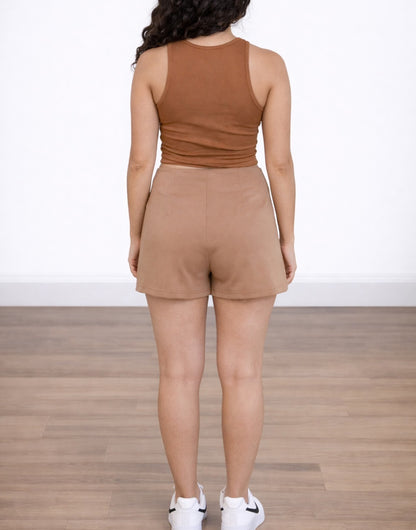 Back view of woman wearing a brown crop tank top and beige Split Hem Knit Skort with wooden floor and white background